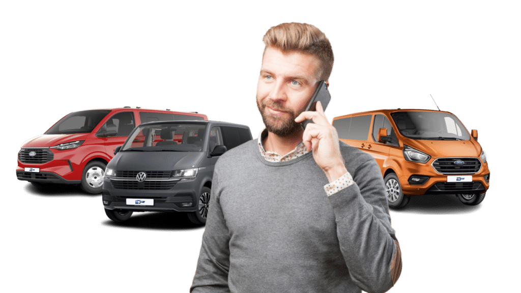 ein mann gekleidet mit einem grauen pullover und hemd telefoniert, im hintergrund stehen 3 9-sitzer der marke ford und vw